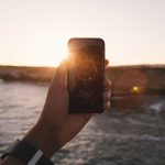 Un cellulare in mano che fotografa un tramonto sul mare