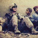 Un soldato seduto in terra circondato da tre bambini e un cane